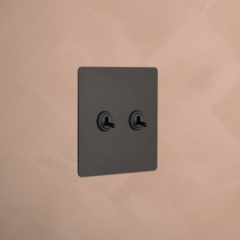 A minimalist beige  light switch plate with two round toggle switches, mounted on a soft pink  wall.