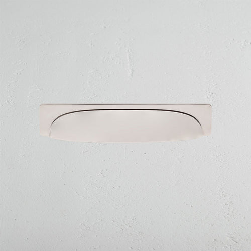 Elm Cup Handle Medium in polished nickel, curved and recessed, mounted on a white textured wall.
