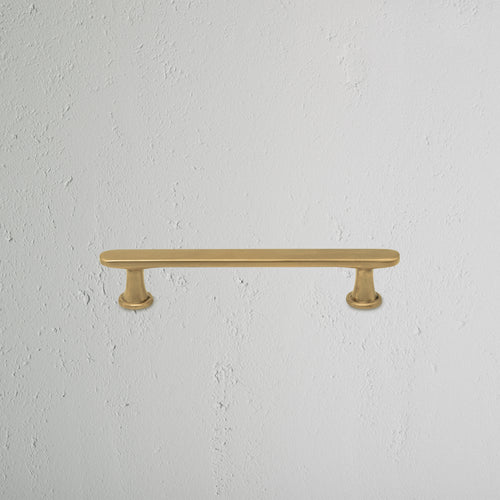 Milliner Furniture Handle Small in antique brass with rounded ends, mounted on a white textured wall.