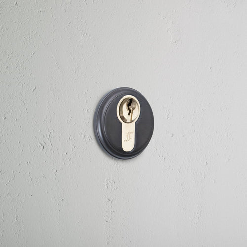 Bronze Canning Key Escutcheon with a circular design, mounted on a light gray textured wall.