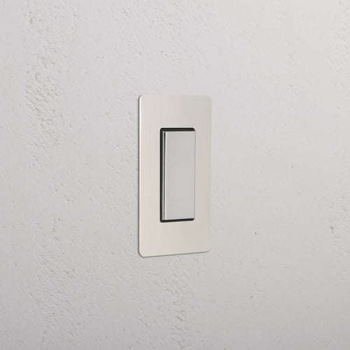 Kew 1G Center Retractive Rocker Switch in polished nickel black, installed on a white textured wall.