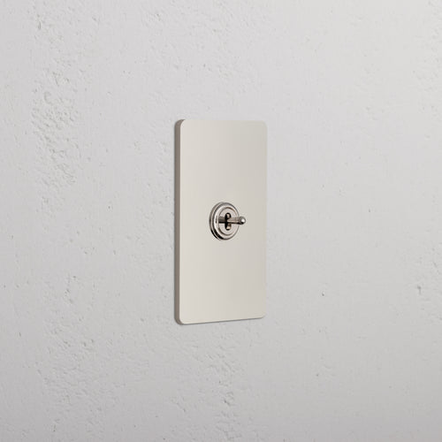 Grove 1G Center Retractive Toggle Switch in polished nickel with single toggle on a white textured wall.