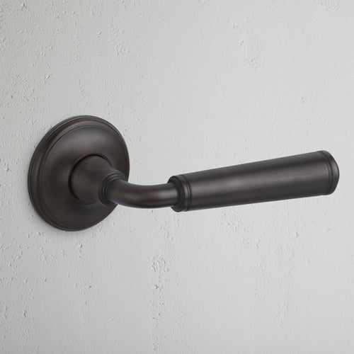 Bronze Digby Passage Door Handle Unsprung with a round base plate, mounted on a light wall.
