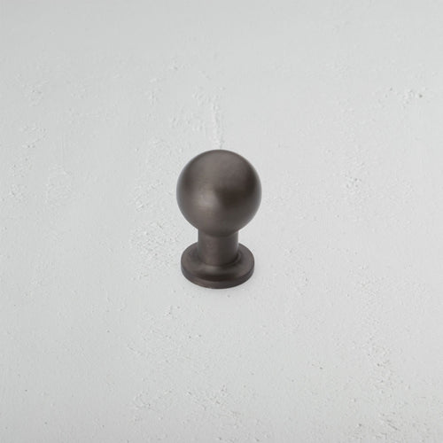 Small round bronze Bayswater Furniture Knob with a short cylindrical base on a white textured surface.