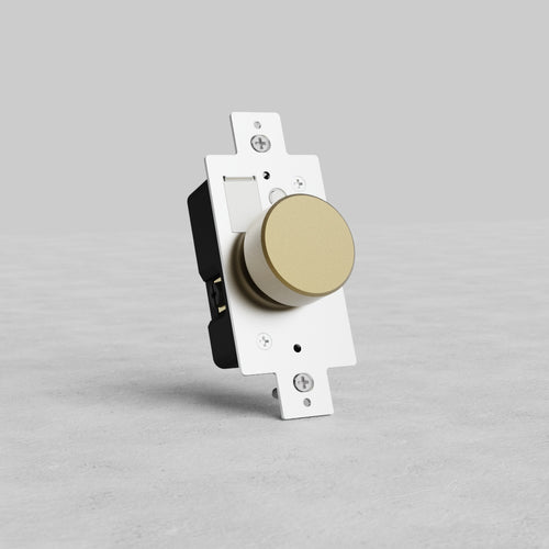 Antique Brass dimmer switch with a gold round knob on a rectangular white faceplate, upright on gray surface.