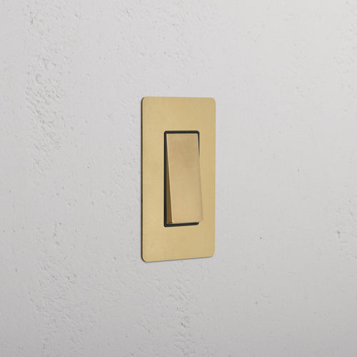 Kew 1G Rocker Switch in Antique Brass Black finish, shown installed on a white wall, switch off.