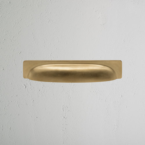 Elm Cup Handle Medium in antique brass finish, featuring a smooth curved design on a light gray surface.