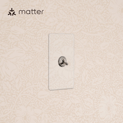 Kew 1G Smart Retractive Toggle Switch in clear polished nickel, mounted on a wall with floral wallpaper.