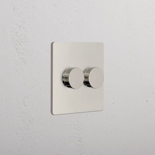 Grove 2G Dimmer Switch in polished nickel with two round knobs, shown mounted on a white wall.