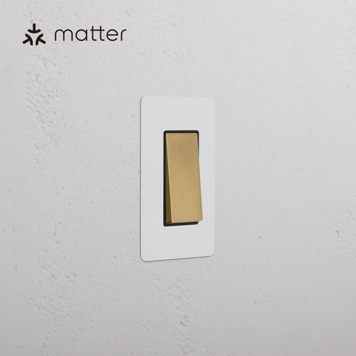 Kew 1G Smart Retractive Rocker Switch, Paintable Antique Brass Black, mounted on white textured wall.