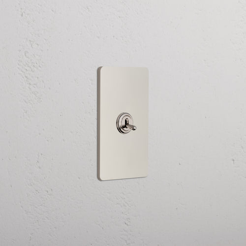 Grove 1G Dimming Retractive Toggle Switch in polished nickel, shown mounted on a white wall.