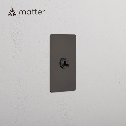 Bronze Kew 1G Smart Retractive Toggle Switch mounted on a white textured wall, Matter logo visible.