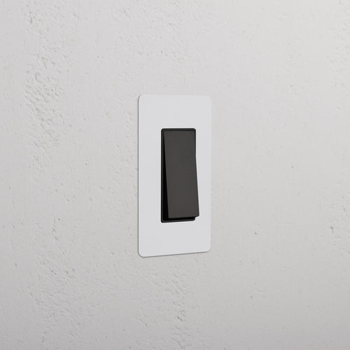 Kew 1G Retractive Rocker Switch in paintable bronze black finish, installed on a white wall plate.