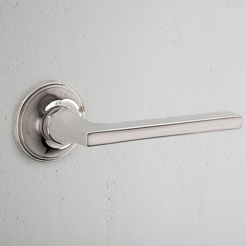 Clayton Passage Door Handle Set in polished nickel with a round base, mounted on a light gray wall.