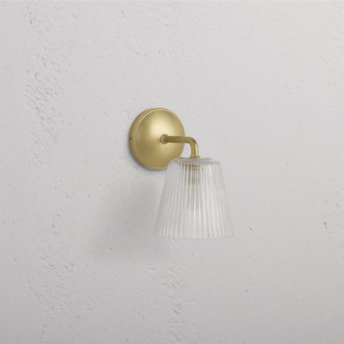 Richmond Medium Wall Light with fluted clear glass shade and antique brass base mounted on a white wall.