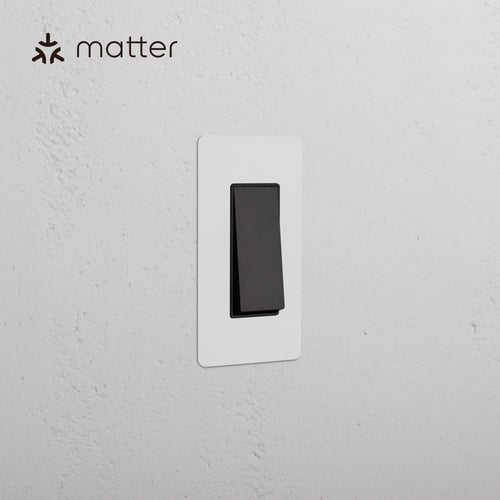 Kew 1G Smart Retractive Rocker Switch in Paintable Bronze Black, shown with a white cover plate on a white wall.