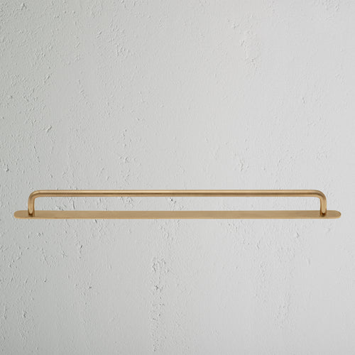 Large antique brass Kilburn furniture handle with rounded ends, mounted on a white textured surface.