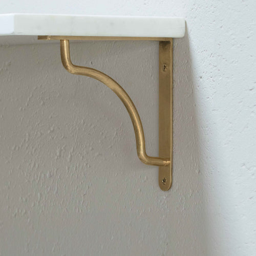 Small Kilburn Shelf Bracket in antique brass with a curved design, mounted on a light textured wall.