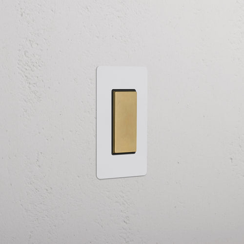 Kew 1G Center Retractive Rocker Switch in paintable antique brass black, shown installed on a white wall.