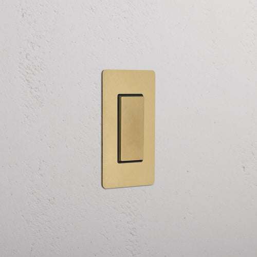 Kew 1G Center Retractive Rocker Switch in Antique Brass Black, rectangular plate, mounted on wall.