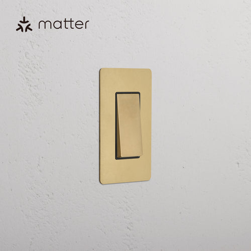 Kew 1G Smart Retractive Rocker Switch in Antique Brass Black, shown mounted on a textured white wall.