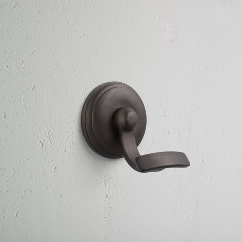 Portland Hook in bronze finish, featuring a curved design, mounted on a light grey textured wall.