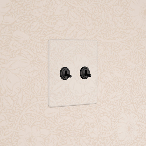 Kew 2G Toggle Switch - Clear Bronze with two black toggles installed on beige floral-patterned wallpaper.