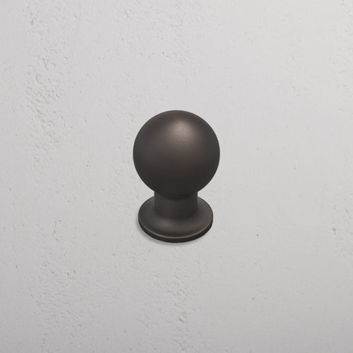 Medium-sized Bayswater Furniture Knob in matte bronze, mounted on a textured white wall.