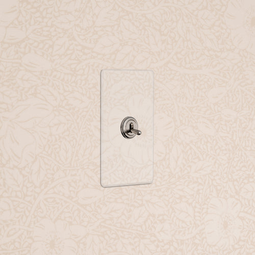 Kew 1G Toggle Switch in Clear Polished Nickel mounted on a wall with cream floral wallpaper.