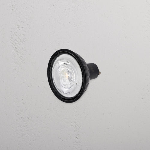 Arthur 11W 70mm LED GU10 24° Bulb in black, shown mounted on a white wall, lens facing outward.