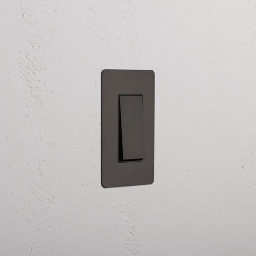 Kew 1G Dimming Retractive Rocker Switch in Bronze Black, mounted on a white textured wall.
