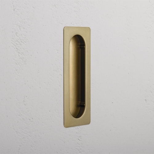 Regent Recessed Medium Pull in antique brass with an oval inner grip, mounted on a white textured wall.