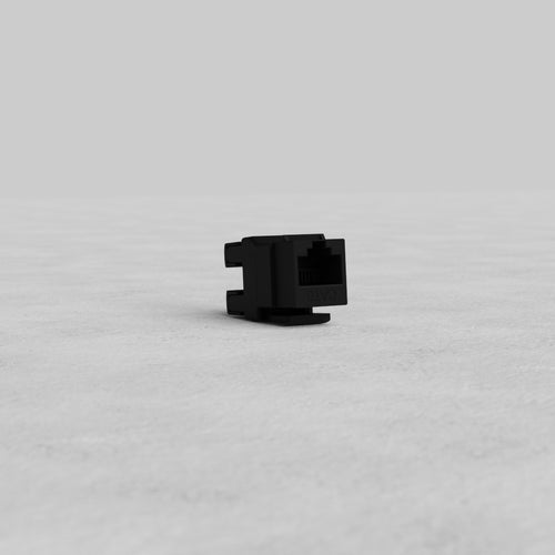 Black CAT 6 Keystone Module displayed on a light gray textured surface with a plain gray background.