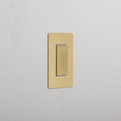 Kew 1G Center Retractive Rocker Switch in Antique Brass White mounted on a white wall.
