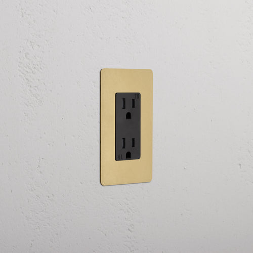 Kew 1G 15A electrical outlet in black with antique brass faceplate, shown on a white wall.
