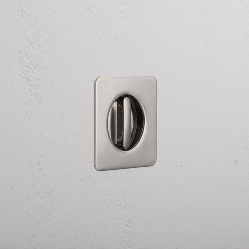 Polished nickel Regent Recessed Thumbturn with square plate, mounted on a white textured wall.