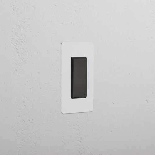 Kew 1G Center Retractive Rocker Switch in Paintable Bronze Black, shown installed on a white wall.