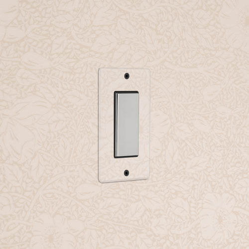 Kew 1G Center Retractive Rocker Switch in clear polished nickel black, mounted on floral wallpapered wall.