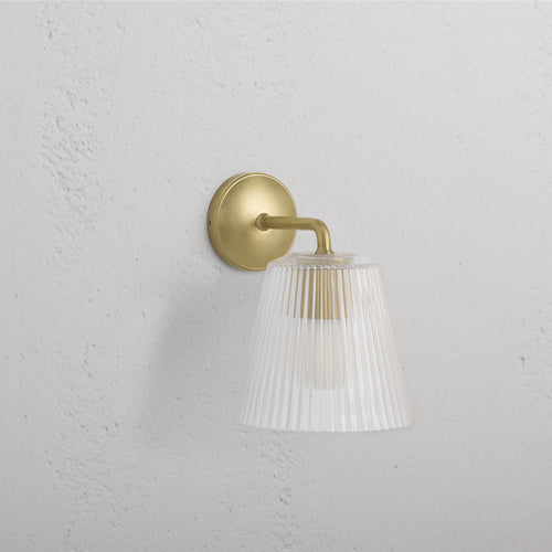 Large Richmond Wall Light in Antique Brass with clear fluted glass shade, mounted on a white wall.