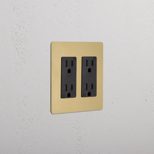 Kew 2G Outlet in Antique Brass Black with two black sockets, mounted on a light textured wall.