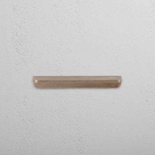 Oxford Furniture Handle Small in antique brass, mounted on a textured white wall.