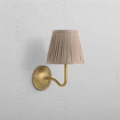 Malvern Medium Wall Light in antique brass with a pleated natural beige shade mounted on a wall.