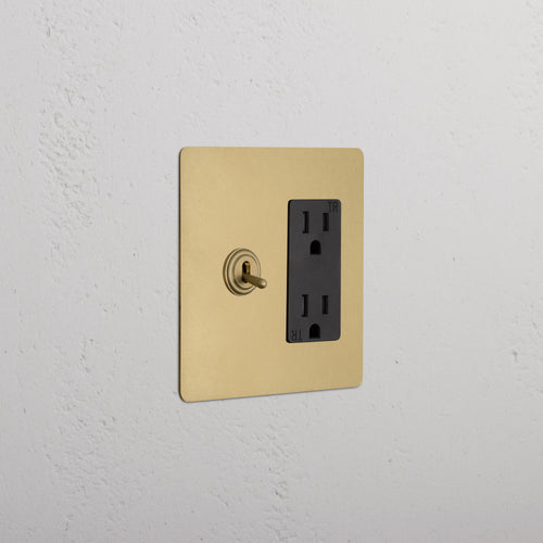 Kew 2G Toggle Switch & Outlet in Antique Brass Black with two toggle switches and dual power sockets on a wall.
