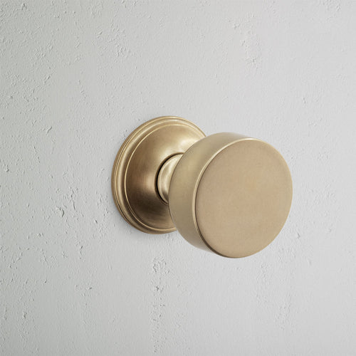 Onslow Passage Door Knob Set in Antique Brass mounted on a light grey textured wall.