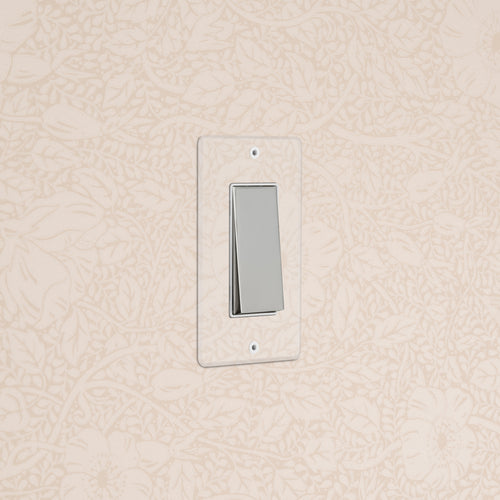 Kew 1G Rocker Switch in clear polished nickel with white insert, mounted on floral-patterned wallpaper.