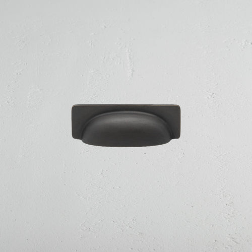 Elm Cup Handle Small in bronze finish, cup-style drawer pull mounted on a white textured surface.
