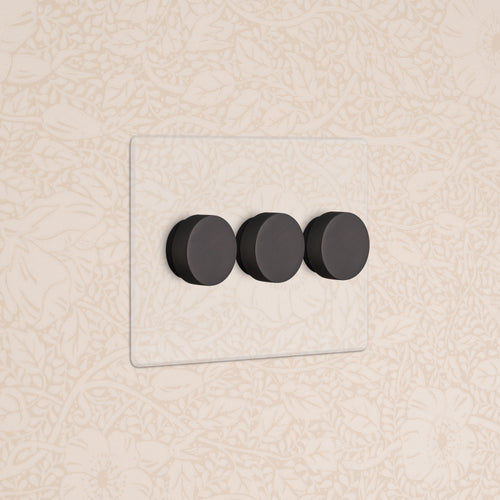 Kew 3G Dimmer Switch in Clear Bronze with three black dials, mounted on a beige floral-patterned wall.