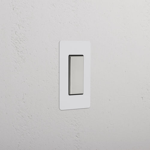 Kew 1G Center Retractive Rocker Switch in paintable polished nickel black, shown on a white wall.