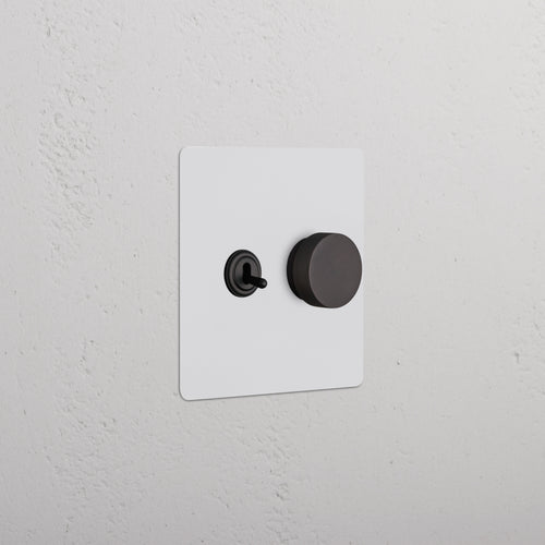 Kew 2G Toggle & Dimmer Switch in paintable bronze, with black toggle and round dimmer knob on white wall.