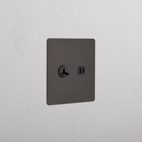 Kew 2G Toggle Switch & Fast Charge USB in bronze black with toggle levers and USB ports on a white wall.